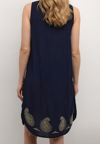 Marineblaues ärmelloses Kleid mit lockerer Passform, das am Saum mit goldenen Paisleymustern bestickt ist und aus einem glatten, strukturierten Stoff besteht.