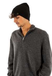 Czarna, prążkowana czapka noszona z szarym swetrem zapinanym na zamek. Sweter jest miękki, o teksturowanym wykończeniu i wygodnym kroju.