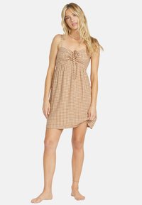 Ruutukuosiset beige ja ruskeat mini-mekko säädettävillä ohuilla olkaimilla ja edessä olevan solmun yksityiskohdan kanssa, jossa on rento malli ja lentävä kangas.