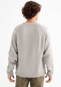 Suéter de punto gris claro con puños y dobladillo acanalados, con cuello redondo y un corte relajado, que muestra un diseño de tejido texturizado.