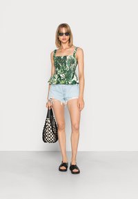 Top peplum com padrão de folhas verdes e decote quadrado, calções de ganga azul claro, sandálias pretas de deslizar e uma bolsa tecida em preto e creme.