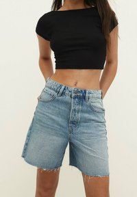 Top negro corto con mangas cortas combinado con pantalones cortos de mezclilla de cintura alta en un tono azul claro, con dobladillo deshilachado y diseño de cinco bolsillos.