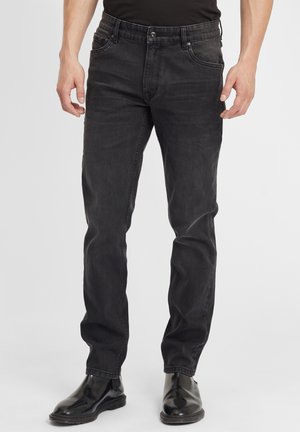 Musthave teksast, sirgedenim püksid sirge sääre disainiga, nupuga kinni keeratav ja viie taskuga, koos mustade nahast saapatega. Sile tekstuur.