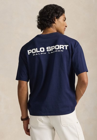 Μπλε βαμβακερό t-shirt με κοντά μανίκια, με μεγάλες λευκές επιγραφές "POLO SPORT" και "RALPH LAUREN" στην πλάτη. Απλό σχέδιο, άνετη εφαρμογή.