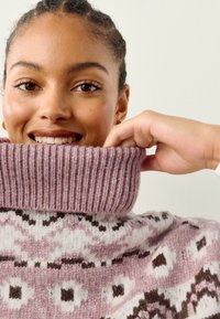 Gebreide trui met een opgerolde geribbelde kraag in lichtroze. Heeft een geometrisch patroon in wit en bruin. Zachte textuur en een ontspannen pasvorm.