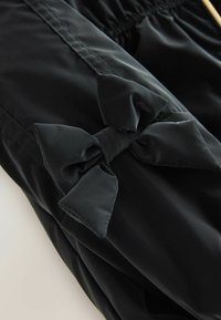 Tessuto di raso nero con una cintura arricciata. Presenta un prominente accessorio a forma di fiocco nero. Texture liscia e design elegante.