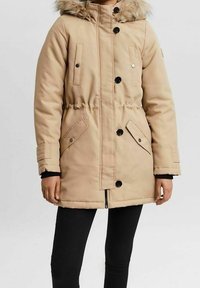 Parka beige con cappuccio in pelliccia sintetica, chiusura con bottoni e zip, tasche laterali, vita elasticizzata e texture trapuntata.