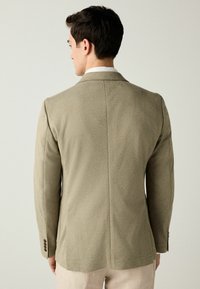 Olivgrüner Blazer mit glatter Textur, tailliertem Schnitt und Reverskragen. Verfügt über drei Knöpfe an den Ärmeln und eine gerade Naht hinten.