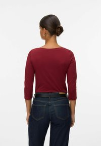Bordeaux langsl sleeve top met een brede halslijn, gecombineerd met donkere spijkerbroek en een zwarte riem, met een getailleerde vorm en een soepele textuur.