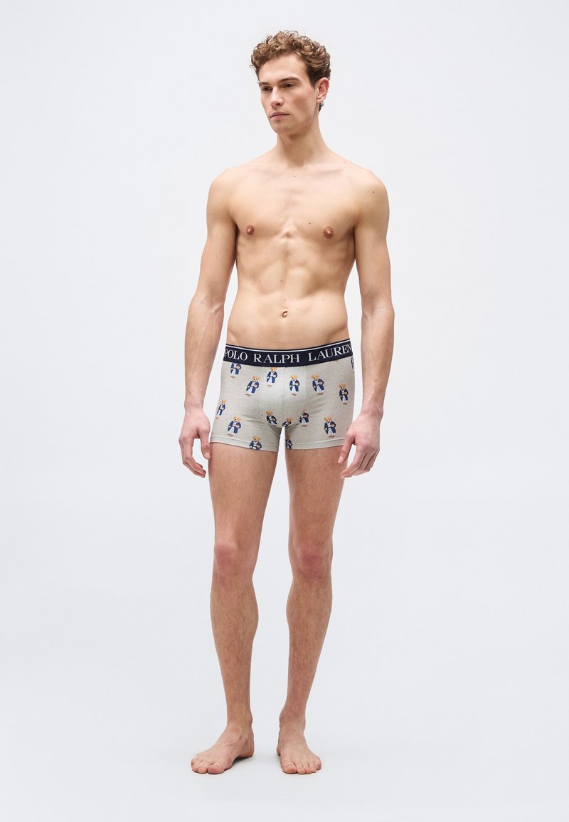 Άνδρας μοντέλο χωρίς πουκάμισο στέκεται, φορώντ ας μπεζ μποξεράκια με τύπωμα αρκούδας και λάστιχο μέσης με την επιγραφή "Polo Ralph Lauren" σε απλό φόντο.