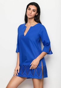 Vestido azul de túnica hecho de tela ligera, con escote en V, mangas tres cuartos y un dobladillo de encaje con corte y un patrón geométrico.