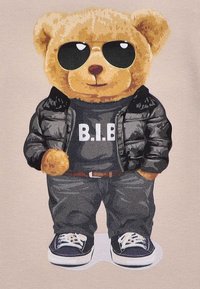 Teddy-Bär-Charakter, der eine schwarze Daunenjacke, ein graues Shirt mit dem Text "B.I.B.", passende Hose und marineblaue Sneakers mit weißen Sohlen trägt.