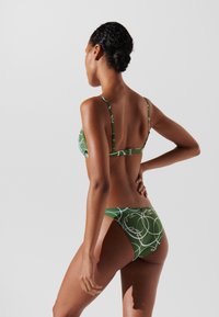 Žalias bikini rinkinys su baltais sukimosi raštais. Viršus turi reguliuojamus petnešas ir užsegimą nugaros pusėje; dugnai turi vidutinio aukščio kirpimą.