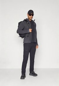 Juoda lauko apranga, įskaitant striukę su užtrauktuku, ilgomis rankovėmis marškinėlį, krovinių kelnes ir žygiavimo batus. Aksesuarai: kuprinė ir saulės akiniai.