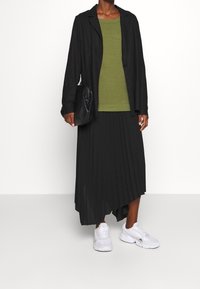 Czarna, oversize'owa marynarka, oliwkowy, fakturowany sweter, plisowana czarna spódnica i białe trampki. Torebka o gładkiej, czarnej fakturze.