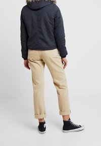 Mørk polstret jakke med prikker, pelsforet hætte og elastiske manchetter; parret med opsmøgede khaki bukser og sorte høj-top sneakers.