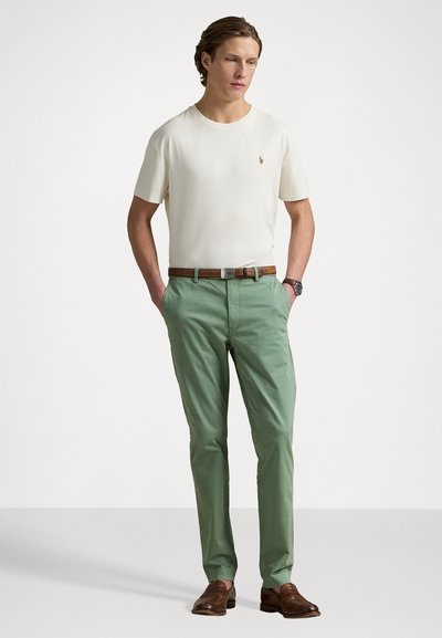 Vaahto beiges suorassa hihassa paidassa, slim-fit mintunvihreissä housuissa, ruskeassa nahkavyössä ja samanvärisissä loafereissa. Yksinkertainen muotoilu ilman kuvioita.