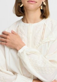 Weiße Bluse mit strukturiertem Stickerei, Spitzenakzenten und Knopfverschluss, mit gerafften Ärmeln und einem weichen, leichten Stoff.