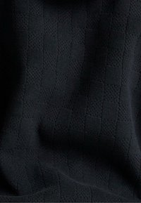 Schwarzer Stoff mit einem subtilen Schachbrettmuster, das aus abwechselnd glatten und strukturierten Quadraten besteht.