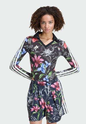 Kvinde med krøllet hår iført sort blomsterprintet langærmet top og matchende shorts med hvide striber og farverige blomsterprint.