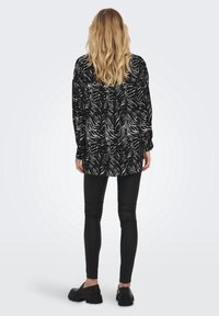 Zwart-witte langemouwen shirt met een zebra-patroon, gecombineerd met zwarte leggings en chunky zwarte schoenen. Glad materiaal met een comfortabele pasvorm.