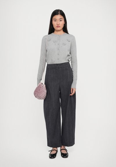 Pulover gri cu textură florală, nasturi, asortat cu pantaloni largi gri închis și o geantă roz cu textură. Pantofi negri cu fundițe.