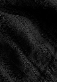 Gros plan sur un tissu noir avec des coutures texturées en diagonale et des fibres tissées visibles créant un motif de lignes en relief.
