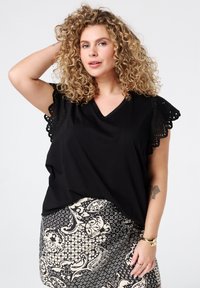 Haut noir à manches courtes avec un col en V et une décoration en dentelle sur les manches, associé à une jupe à motifs présentant des dessins floraux et géométriques.