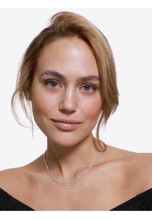 Collier en argent à plusieurs couches, orné de fines perles cylindriques et d'une finition polie, reposant au-dessus d'une clavicule découverte.