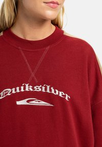 Bordeaux sweatshirt met een ronde hals, tan accenten op de schouders en een geborduurd "Quiksilver" logo met een golfontwerp.