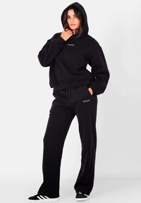 Zwarte hoodie met een ontspannen pasvorm, voorzien van een klein logo. Gecombineerd met bijpassende zwarte joggingsbroek, ook met een logo.