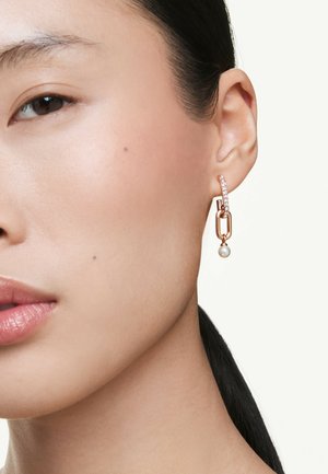Orecchino in metallo dorato con un design a catena, caratterizzato da una goccia di perla e accenti di cristallo trasparente lungo l'anello.