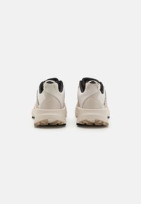 Chaussures de sport avec un design beige et noir, dotées d'un col rembourré, de semelles texturées et d'un logo sur le côté.