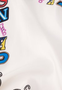 Tela blanca con letras y símbolos estilizados multicolores en diversas tipografías y tamaños, con una textura suave y un ligero brillo.