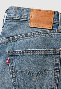 Jean en denim bleu clair avec une patch en cuir portant l'étiquette "Levi Strauss & Co." au niveau de la taille, présentant des coutures contrastantes orange et des poches arrière.
