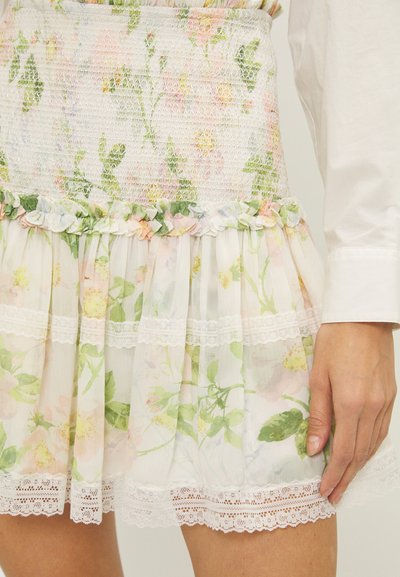 Blomstrete kjole med smock-bodice i pastellfarger, med volangkant og blonder. Laget av lette stoffer med et gjennomsiktig lag.