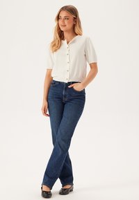 Kortärmad vit cardigan med knäppning framtill, texturerat tyg, i kombination med blå denim jeans med utsvängda ben och svarta ballerinas. Lätt avslappnad passform.