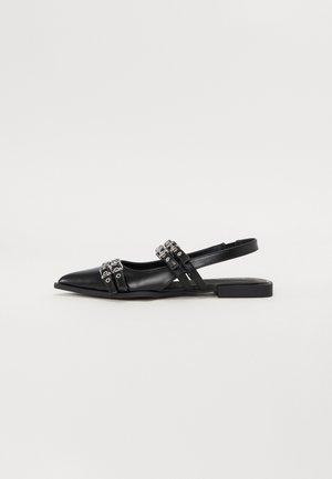 Chaussure plate noire à bout pointu type slingback avec deux brides décoratives à boucles argentées sur le devant et une bride arrière ouverte.