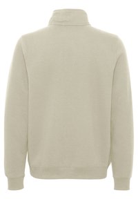 Suéter de color beige claro con un cuello alto, mangas largas y puños acanalados. Fabricado en un suave tejido con costuras mínimas y una textura lisa.