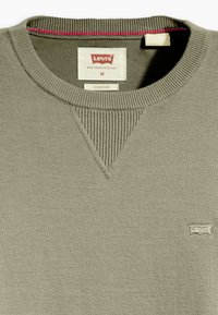 Olijfgroen trui gemaakt van zachte stof. Heeft een geribbelde halslijn en schouderaccenten, met een klein Levi's logo op de borst.