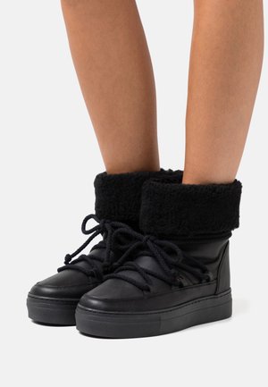 Bottines noires à cheville avec un revers en fausse fourrure, des lacets épais et une semelle en caoutchouc texturée. Tige en cuir lisse avec un col rembourré pour le confort.