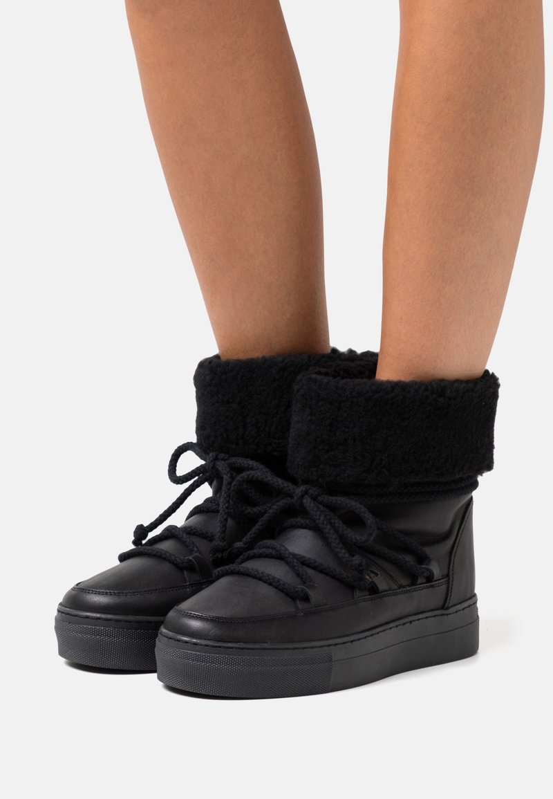 Bottines noires à cheville avec un revers en fausse fourrure, des lacets épais et une semelle en caoutchouc texturée. Tige en cuir lisse avec un col rembourré pour le confort.