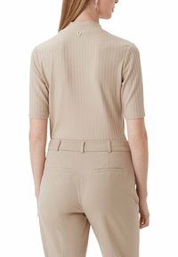 Krótki rękaw, prążkowany top w jasnym beżu, z wysokim kołnierzem i małym guzikiem z tyłu. Zestawiony z jasnobeżowymi spodniami od garnituru.
