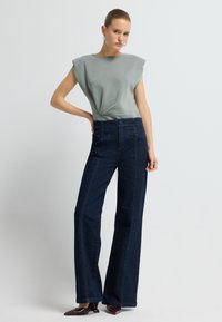 Světle šedý top s krátkými rukávy a stříbrně zvýrazněným výstřihem, doplněný o tmavě modré široké džíny s vysokým pasem a kapsami.