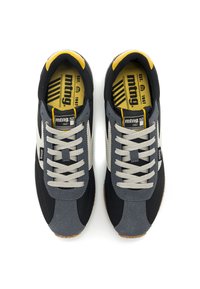 Schwarze und graue Sneakers mit einem Obermaterial aus Wildleder und Mesh, ausgestattet mit grauen Schnürsenkeln, einem weißen Seitlogo und einem gelben Akzent am Kragen.