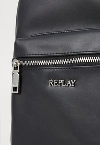 Zaino sintetico nero con cerniera argento, superficie texturizzata e logo "REPLAY" ben visibile.