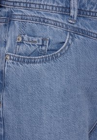 Jeans de mezclilla azul con un acabado texturizado, bolsillo frontal y costuras visibles con acentos de Hardware metálico.