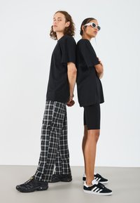 T-shirts en coton noir, pantalons à carreaux à jambes larges et shorts de cyclisme noirs. Les accessoires incluent des lunettes de soleil blanches et des baskets noires avec des rayures.