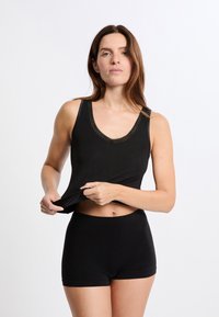 Top corto nero con scollatura a V e rifinitura texturizzata, abbinato a pantaloncini a vita alta coordinati, in tessuto morbido, design aderente.