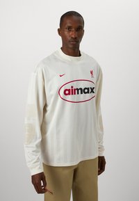 T-shirt a maniche lunghe in jersey color crema con logo rosso, strisce verticali e dettagli testurizzati sulle maniche. Marchio Nike sul petto.